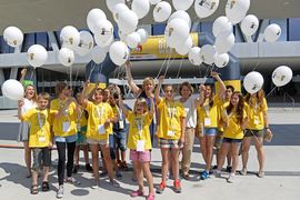 Kinder in gelben T-Shirts halten weiße Ballons in die Luft.