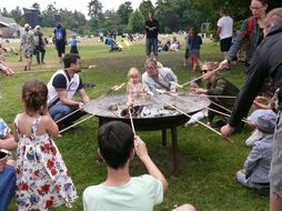Besucherinnen und Besucher grillen Stockbrot über offenem Feuer beim Familientag in Grafenegg