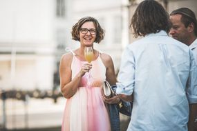 Eine Frau mit einem Glas in der Hand lacht beim Sommerausklang an der Donau-Universtität Krems in die Kamera