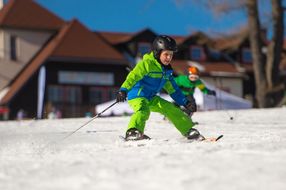 Bub in grünem Ski-Overall fährt Ski.