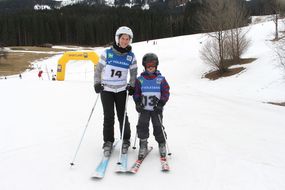 Eine Dame und ein Kind lachen auf Skiern in die Kamera