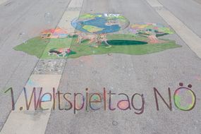 Gemälde aus Kreide mit der Aufschrift "1. Weltspieltag NÖ" auf dem Asphalt.
