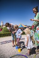 Bub geht an der Hand von einer Dame mit bunten Stelzen beim NÖ Familienfest auf der Schallaburg 2018