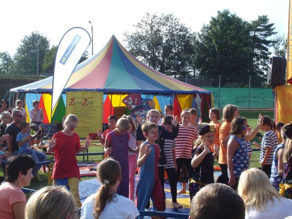 Kinder präsentieren das von ihnen einstudierte Zirkusstück vor einem bunten Zelt