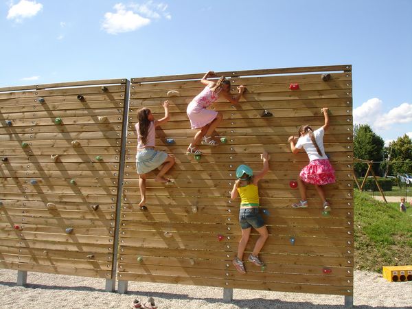 Vier Kinder klettern auf einer Kletterwand aus Holz bei strahlend blauem Himmel