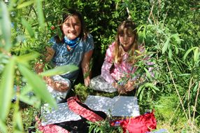 Zwei Mädchen sitzen in einem Weide-Gebüsch