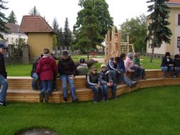 Kinder sitzen auf einer geschwungenen Holzbank in der Wiese