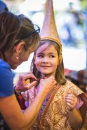 Frau bindet Mädchen beim NÖ Familienfest auf der Schallaburg 2018 einen spitzen Hut unter dem Kinn zu
