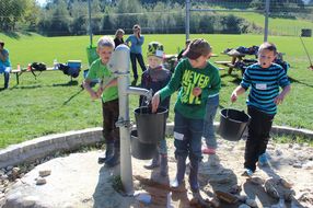 Vier Buben holen beim Brunnen Wasser für die Pflanzen.