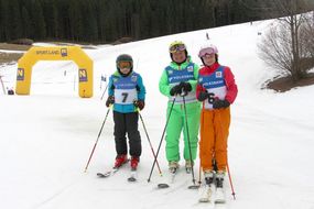 Drei Kinder in Skianzügen lachen in die Kamera