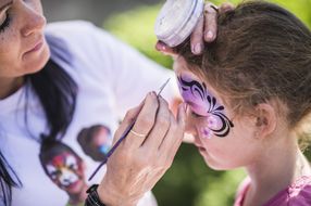 Mädchen wird beim NÖ Familienfest auf der Schallaburg 2018 von einer Frau mit violetter Farbe im Gesicht geschminkt