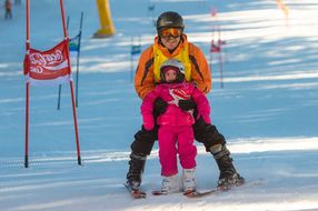 Mann hilft kleinem Kind beim Skifahren