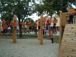Kinder in orangen T-Shirts klettern auf einem Kletter-Parcours aus Holz