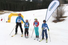 Ein Mann und drei Kinder lachen in voller Ski-Montur in die Kamera