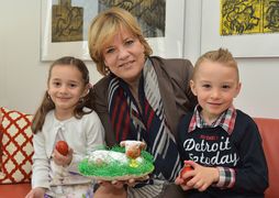 Landesrätin Schwarz hält einen Osterlamm-Kuchen in der Hand und lächelt mit zwei Kindern in die Kamera.